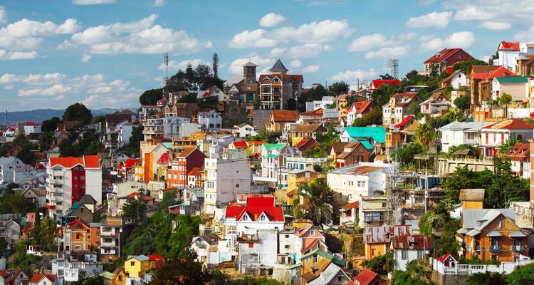 Colorful hillside neighbourhood of Antananarivo with diverse houses under scattered clouds.