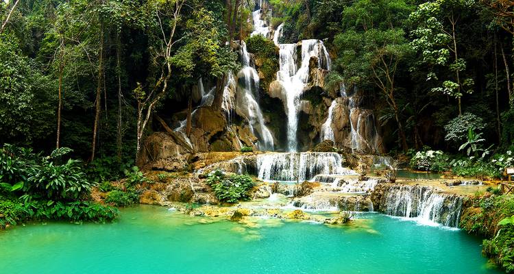 Cascada Kuang Si con múltiples niveles y agua turquesa rodeada de exuberante vegetación.