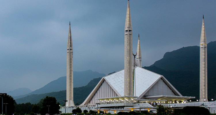 La icónica Mezquita Faisal con sus minaretes elevados y techo triangular blanco se destaca contra las brumosas Colinas Margalla.