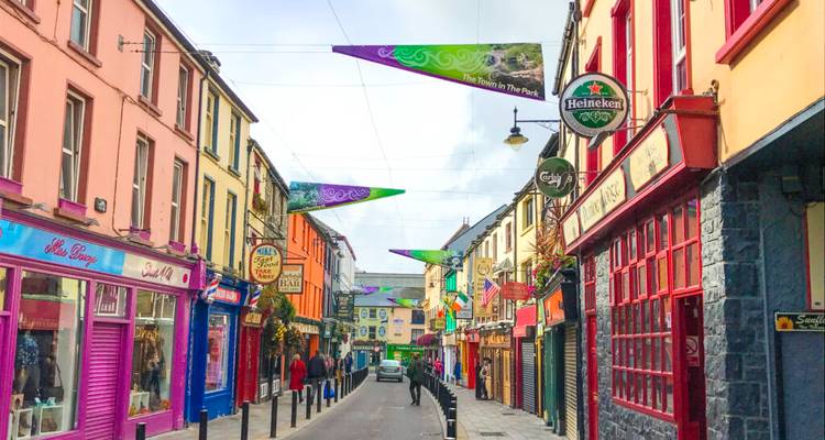 Des façades de magasins colorées bordent une ruelle irlandaise étroite ornée de bannières et d'enseignes de pubs.