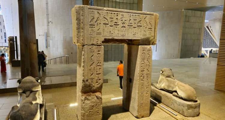 Stone doorway covered in hieroglyphs displayed inside the Grand Egyptian Museum with a visitor in the background.