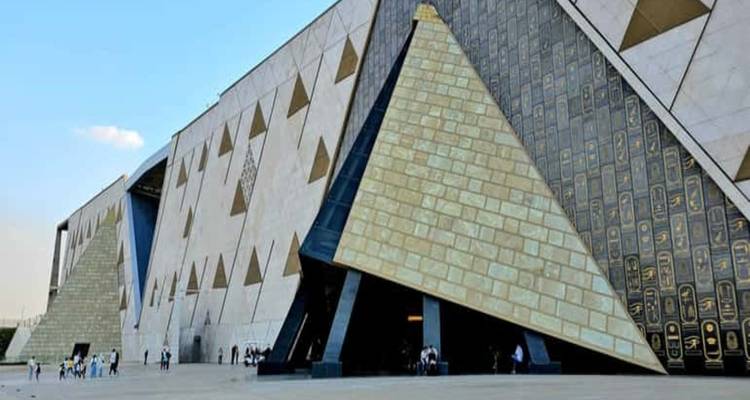 Eckige weiße Steinfassade eines pyramideninspirierten Museumsgebäudes mit kleinen Figuren, die über den offenen Platz gehen