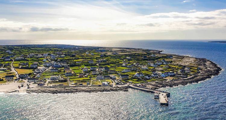 Vue aérienne des champs verts en patchwork de l'île d'Inisheer et de son minuscule port entouré par la mer bleu vif.