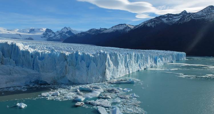 Massive icy wall of Perito Moreno Glacier meeting turquoise waters with mountains beyond.