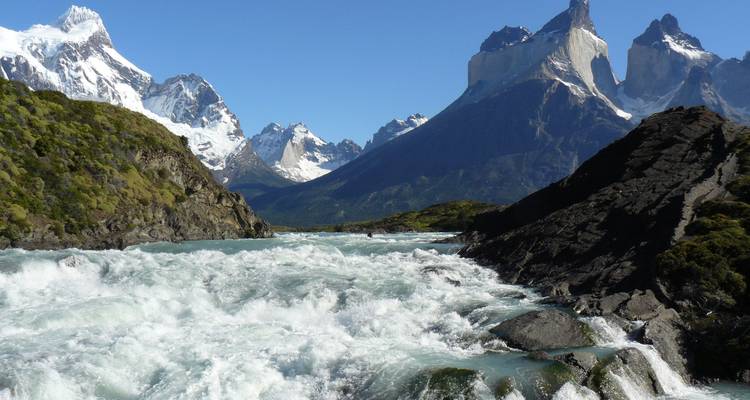 Rushing river with snow-capped Cuernos del Paine peaks towering behind.