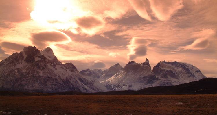 Dramatic Patagonian mountain range at sunset with lenticular clouds glowing orange.