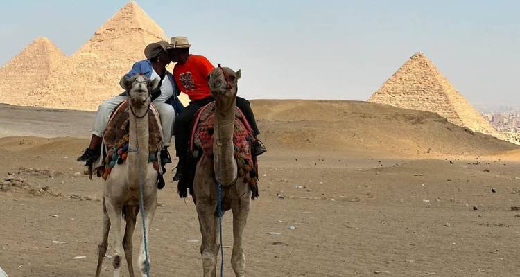 Mensen die op kamelen rijden met piramides op de achtergrond in Giza, Egypte.