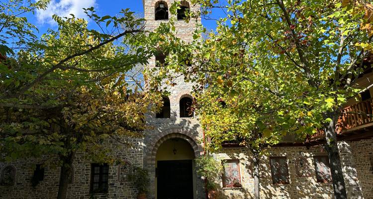 Stone church courtyard shaded by leafy trees with arched entrance and bell tower.