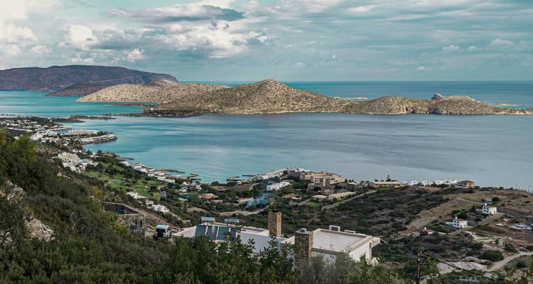 Panorama côtier de la baie d'Elounda et de l'île de Spinalonga avec des collines ondulantes et des villages