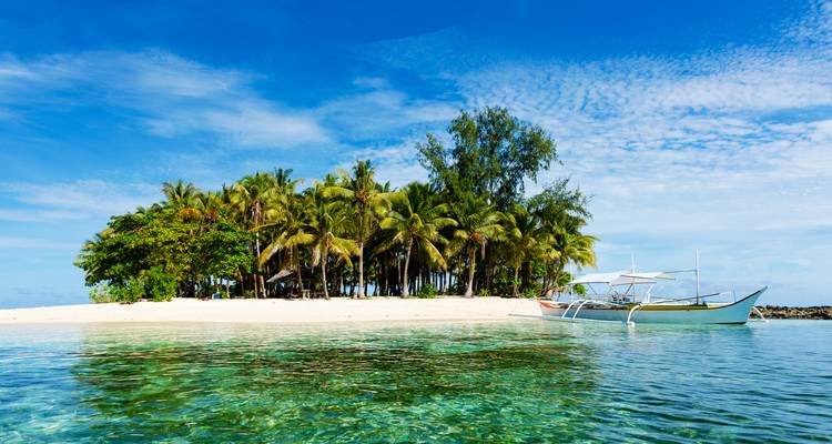 Île tropicale avec des palmiers et un bateau traditionnel flottant sur une eau cristalline.