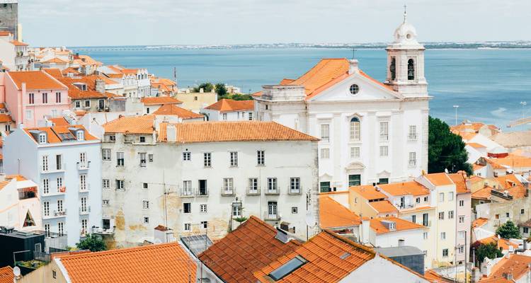 De witte kerk van Lissabon en terracotta daken kijken uit over de brede Taag-estuarium op een zonnige dag.