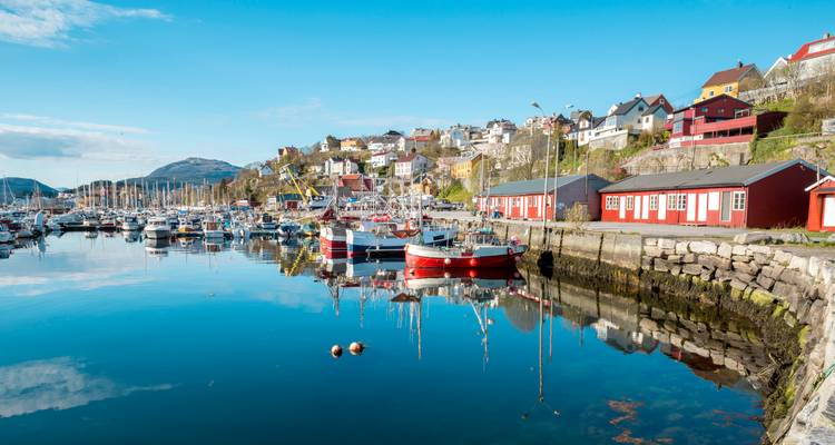 Bright fishing boats and colorful houses reflect in the still harbor water of a Norwegian coastal town.