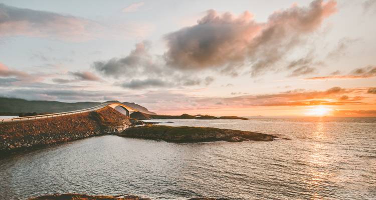 Sunset casts warm light over the sweeping Atlantic Ocean Road curving above island rocks.