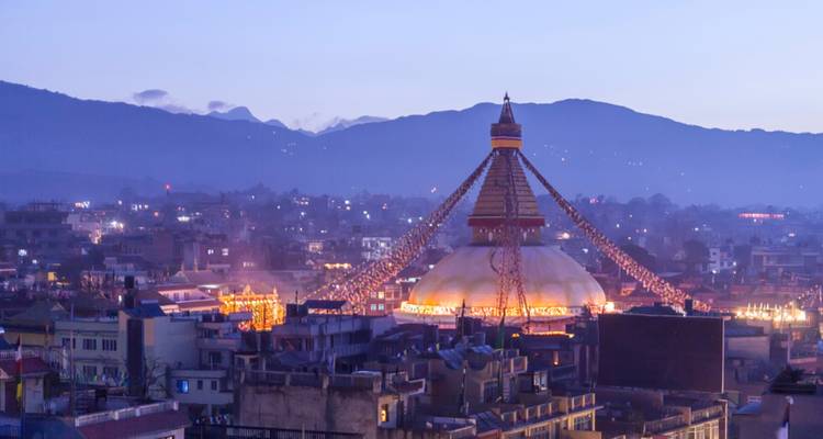 Une vue du stupa de Boudhanath illuminé au crépuscule avec des montagnes en arrière-plan.