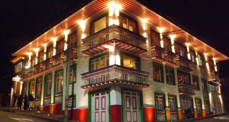 Edificio tradicional colombiano iluminado con luces cálidas contra el cielo nocturno, destacando balcones coloridos y molduras.