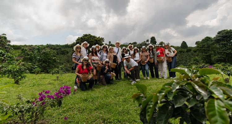 Un grand groupe de touristes portant des chapeaux pose ensemble sur le flanc d'une plantation de café luxuriante sous des nuages dramatiques.