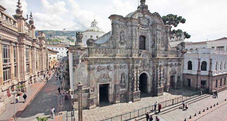 Ornate stone façade of La Compañía de Jesús church on a lively historic street in Quito.
