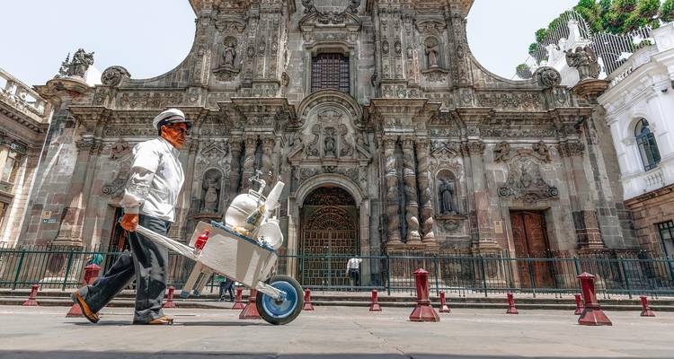 Vendor pushes a metal cart past the detailed stone façade of La Compañía church in Quito’s old town.
