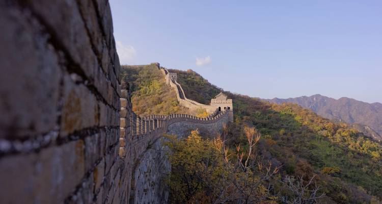 Die Chinesische Mauer schlängelt sich über einen bewaldeten Gebirgskamm unter einem klaren blauen Himmel.