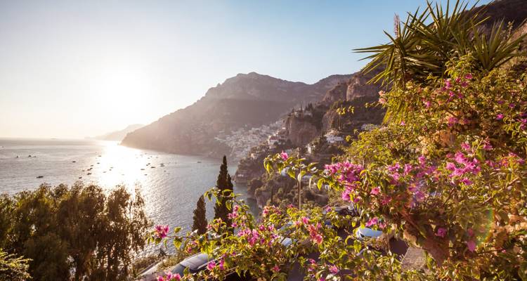 Una vista panorámica de una zona costera con flores y una puesta de sol en Positano, Italia.