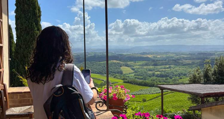 Reiziger die geniet van panoramische uitzichten over glooiende Toscaanse wijngaarden en heuvels vanaf een balkon.