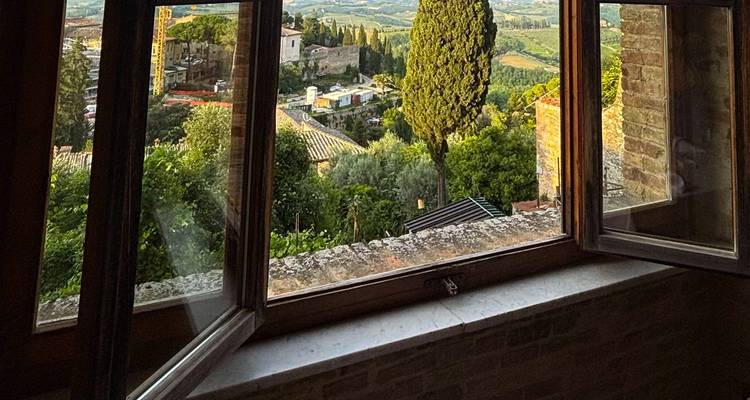 Open raamwerk geeft uitzicht op een schilderachtig Toscaans dorpje met cipressenb0men en glooiende akkerland.