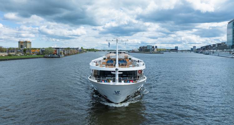 White river cruise ship sailing down a wide waterway under partly cloudy skies