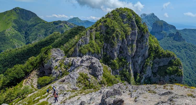 Les randonneurs progressent le long d'une crête calcaire accidentée, entourés de pics verts dentelés et de nuages gonflés au-dessus de leurs têtes.