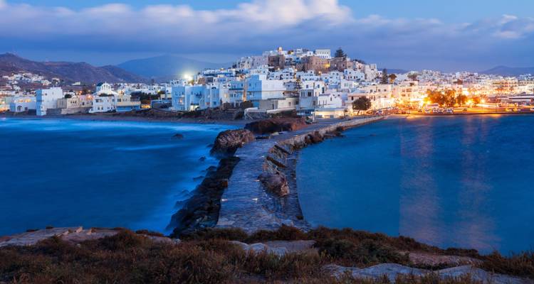 Paisaje urbano insular al atardecer con edificios iluminados sobre el agua.