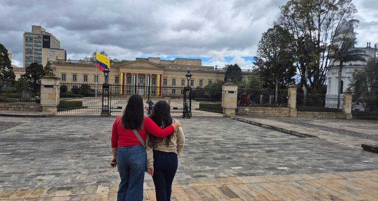 Deux jeunes femmes se tiennent bras dessus bras dessous, regardant vers un imposant palais gouvernemental avec le drapeau colombien.