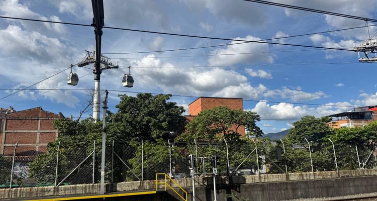 Teleféricos moviéndose a lo largo de cables aéreos contra un cielo azul y un telón de fondo urbano.
