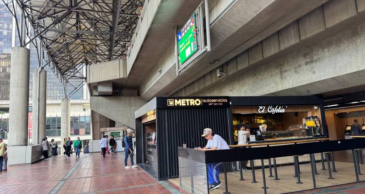 Intérieur d'une station de métro de Medellín avec kiosque, panneaux numériques et voyageurs marchant sur le sol carrelé.