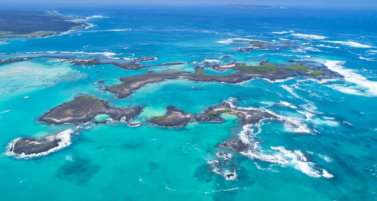 Aerial panorama of turquoise waters and scattered lava islets fringed by white surf in the Galápagos archipelago.