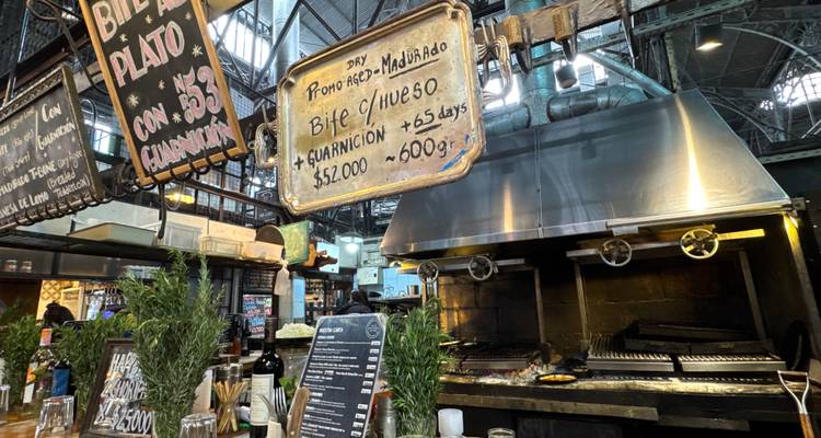 Interieur van een drukke mercado grill met krijttafelmenus en sizzlend vlees boven open vlammen.