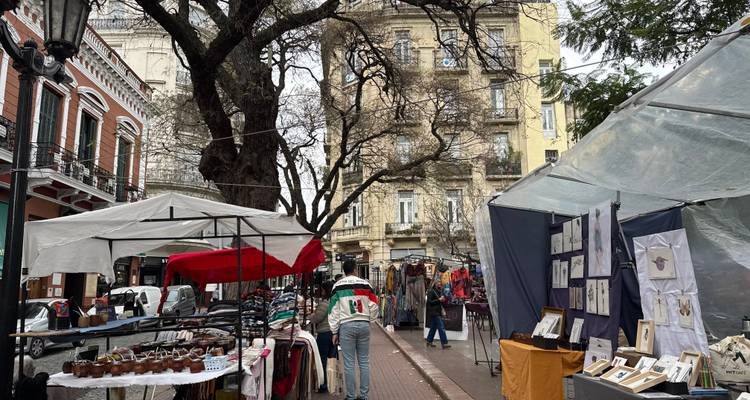 Outdoor ambachtelijke markt in San Telmo met textielkraampjes onder bladrijke bomen en historische gebouwen.