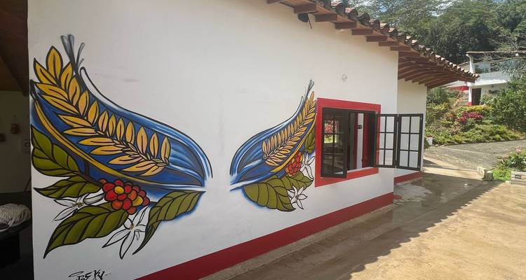 Mural de pared blanca que muestra ramas de café estilizadas formando alas coloridas junto a una ventana.