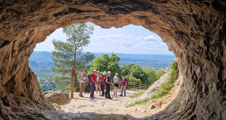 Looking out from a rocky cave mouth to a group of hikers standing at the entrance with panoramic valley views beyond.