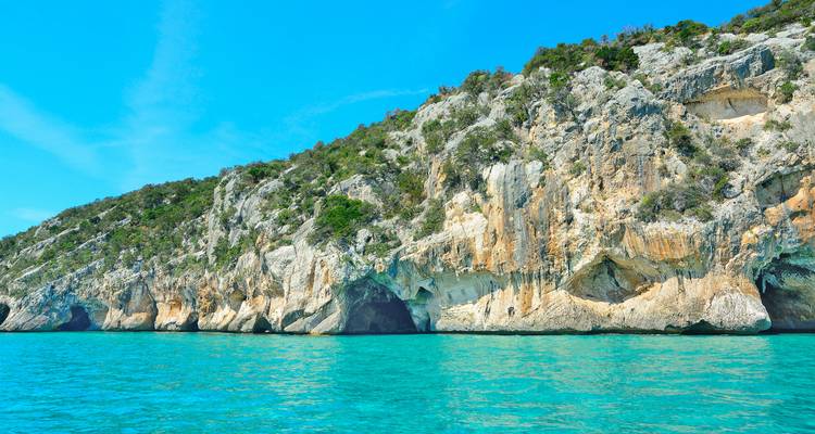 Steep limestone cliffs rising from vivid turquoise Mediterranean waters under a clear sky.