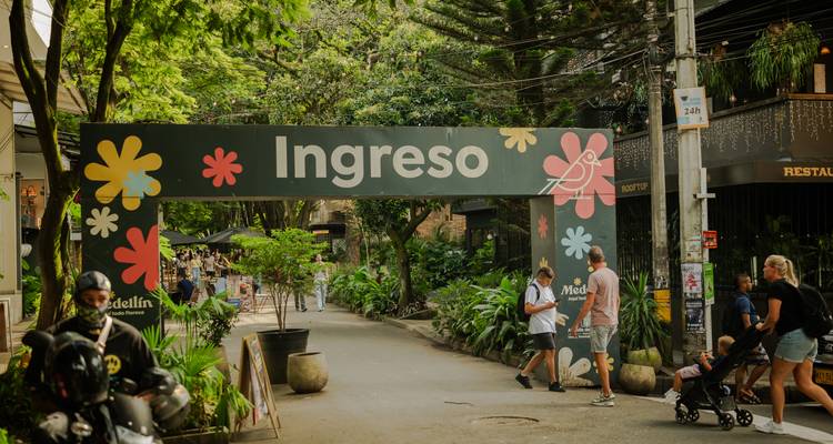 Entrance sign 'Ingreso' to a lively urban park with visitors and lush greenery.