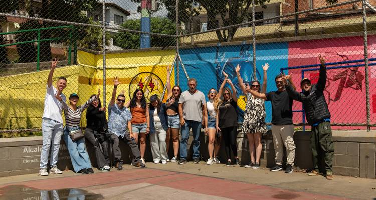 Cheerful tour group with raised arms posing in front of a vibrant court mural.