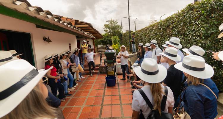 Large group wearing white hats listening to a guide in a courtyard of a rural finca.