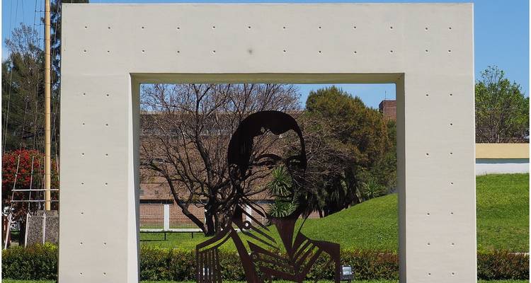 Buste silhouette métallique d'un homme exposé dans un cadre rectangulaire moderne dans un parc urbain verdoyant.