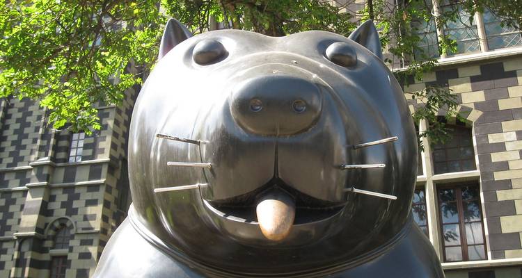Gros plan de la sculpture de chat en bronze brillant de Fernando Botero avec la façade du palais à damier en arrière-plan.