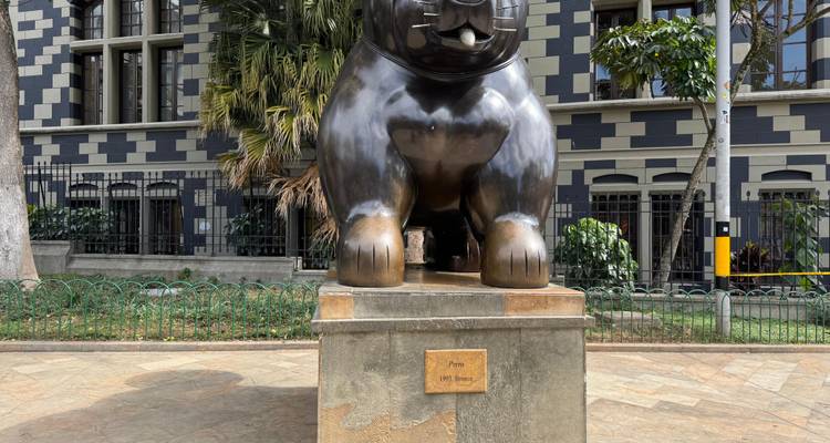 Pattes avant et socle d'une grande sculpture féline en bronze de Botero devant un bâtiment à motifs.