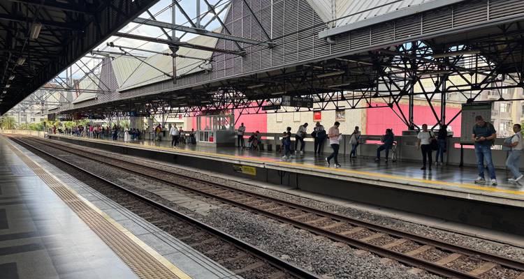 Longue plateforme de métro avec des passagers qui attendent le long des voies ferrées sous une structure de toit métallique.
