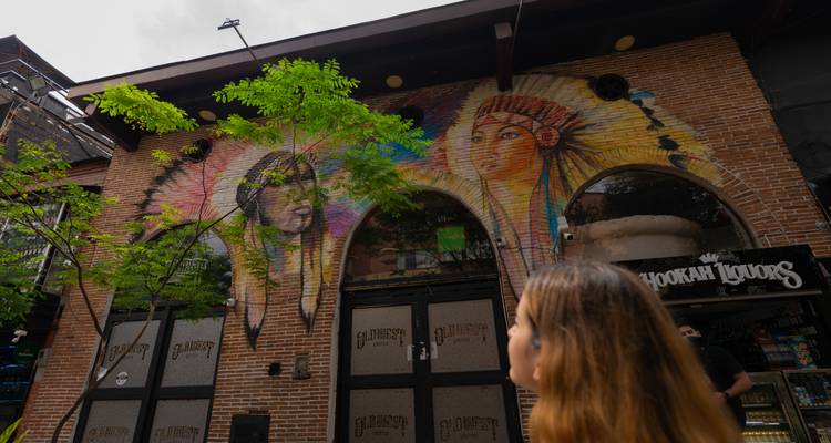 Art de rue aux thèmes autochtones colorés peint sur une façade en brique, avec un passant qui lève les yeux.