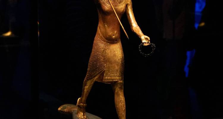 Volledig zicht op een gouden oud-Egyptisch standbeeld in een donkere omgeving.