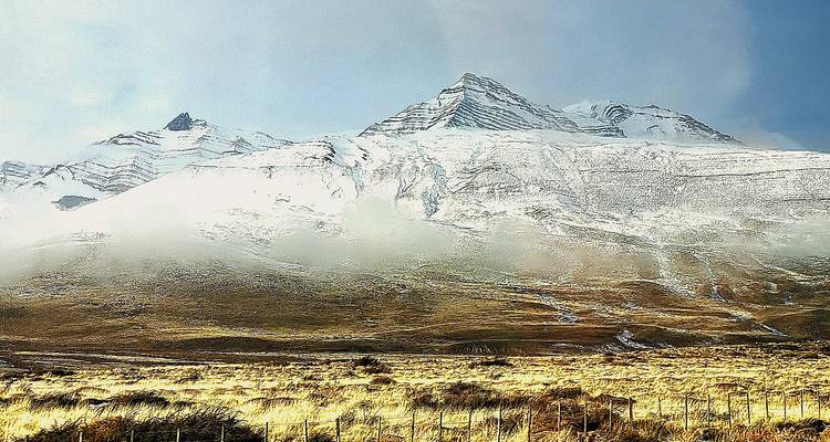 Dramatische puntige besneeuwde top rijst boven de gouden Patagonische steppe uit en wordt gedeeltelijk verscholen door lage wolken.