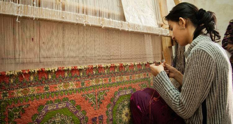 Young craftswoman seated at a loom meticulously weaving a colourful carpet in Uzbekistan.