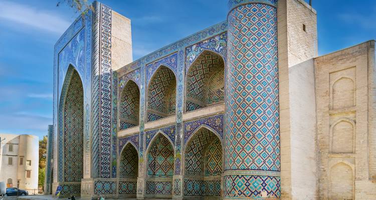 Ornate Timurid madrasa facade covered in intricate blue and turquoise mosaics against a blue sky.